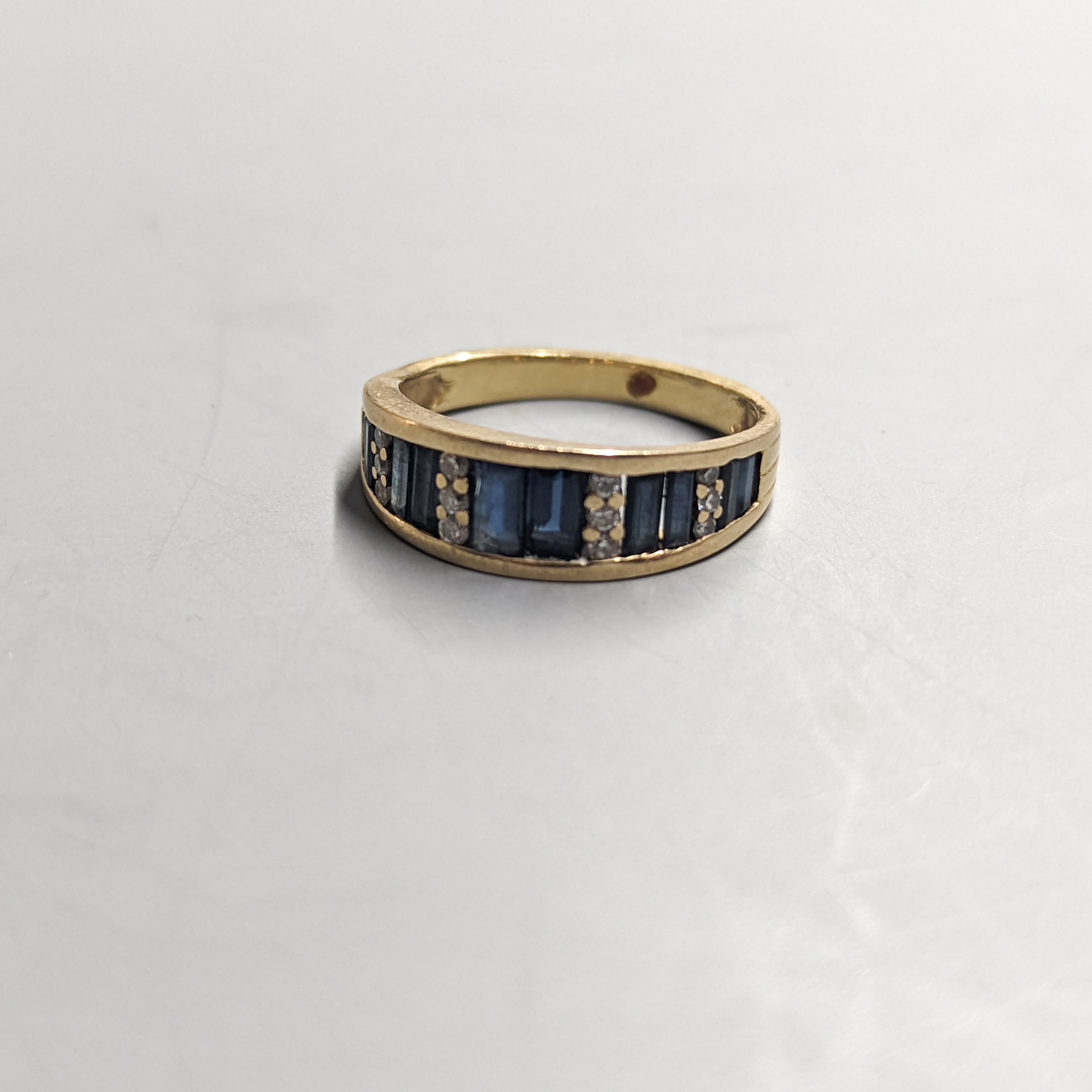 A modern yellow metal, diamond chip and graduated baguette cut sapphire set half hoop ring. size O, gross weight 4.2 grams.